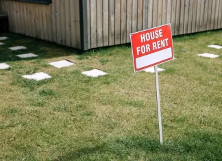 Jak uniknąć problemów z najemcami podczas wynajmu mieszkania Czerwony szyld „House for rent” wbity na trawniku przed domem.